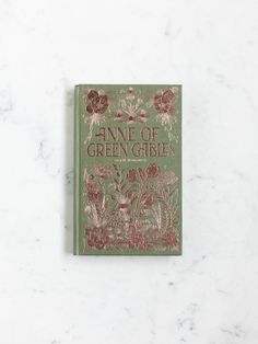 the front cover of an antique book with flowers and plants on it, against a white marble background