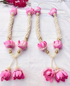 three necklaces with pink flowers and pearls hanging from the sides on a white table