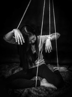 black and white photograph of a woman sitting on the floor with her hands hanging from strings