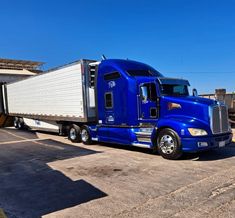 a large blue semi truck parked in a parking lot next to a building on a sunny day