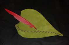 a green hat with a red feather sitting on it's side and a black background