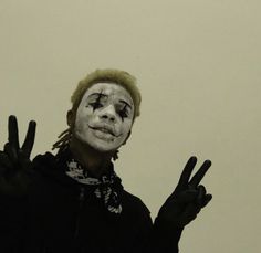 a man with his hands in the air while wearing a clown mask and making peace signs