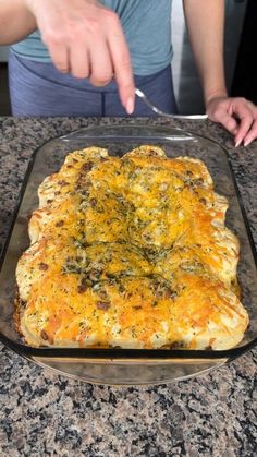 a person cutting into a casserole in a glass dish on top of a counter