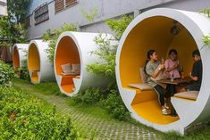 some people are sitting at a table in an unusual looking outdoor area with plants and bushes