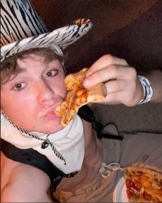 a young man wearing a cowboy hat eating a slice of pizza in front of his face