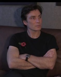 a man is sitting on a couch with his arms crossed and looking off to the side