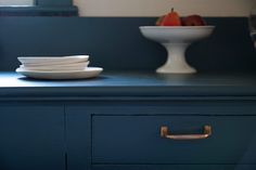 two white plates on top of a blue dresser next to a bowl with an apple in it