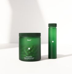 a green jar next to a green container on a white surface with the lid open