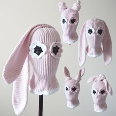 four pink knitted hats with ears and eyes on top of a wooden stand in front of a white wall