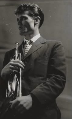 a man in a suit and tie holding a trumpet with his right hand, looking to the side