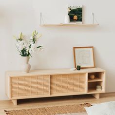 a white vase with flowers on top of a wooden shelf next to a wall mounted art piece