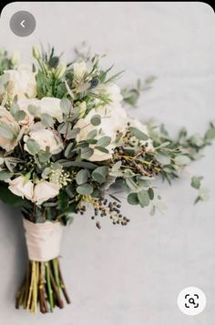 a bridal bouquet with white flowers and greenery on the side of a wall