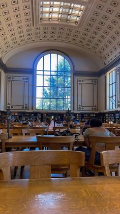 people are sitting at desks in a library with bookshelves and large windows