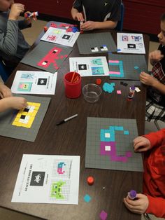 four children are sitting at a table playing with construction paper and colored blocks on it