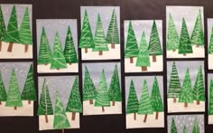 christmas trees made from paper are displayed on the wall in front of a blackboard