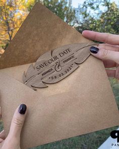 two hands holding an envelope with a wooden save our date stamp on it