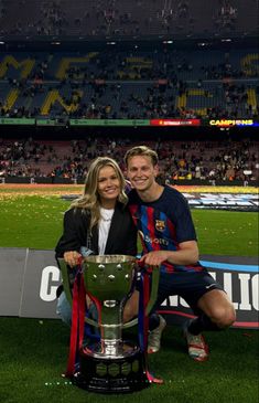 a man and woman sitting on a bench with a trophy in front of them at a soccer game