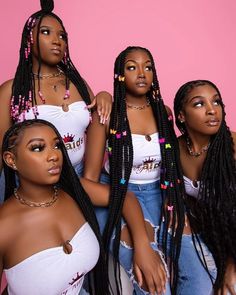 four beautiful women with long braids posing for the camera in front of a pink background