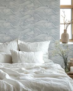 a bed with white linens and pillows in front of a blue wallpapered bedroom