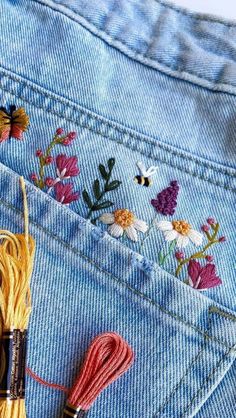 a pair of jeans with flowers on the back pocket and a needle in the front pocket