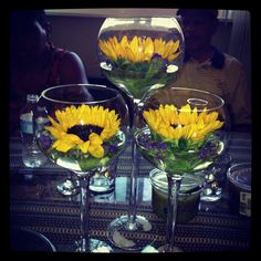 three wine glasses filled with sunflowers on top of a table