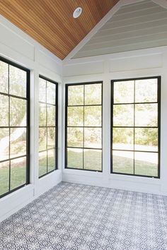 an empty room with large windows and tile flooring on the ground, in front of a wooden ceiling