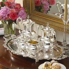 an ornate silver tray with flowers in front of a mirror and vase on a table