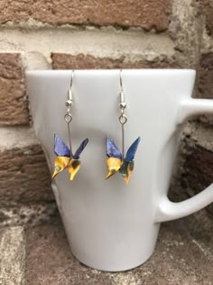 a pair of blue and yellow bird earrings sitting on top of a white coffee cup