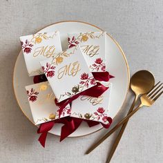 four napkins with gold foil and red ribbon on a plate next to a fork