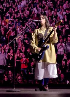 a woman standing in front of a microphone while holding a guitar