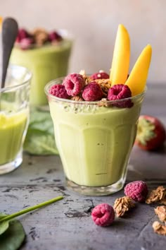 two glasses filled with green smoothie and topped with raspberries