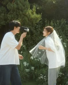 a man and woman standing next to each other with a veil on their head, one holding a hair dryer