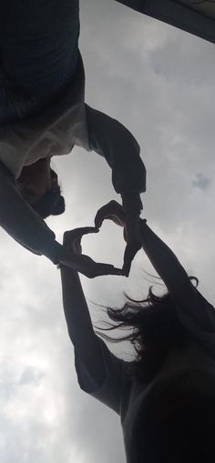 two people holding hands in the shape of a heart with clouds in the sky behind them