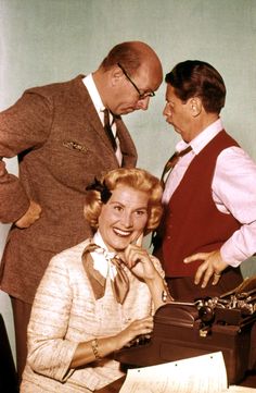 two men and a woman standing next to an old typewriter