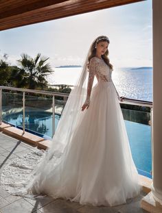 a woman in a wedding dress is standing on the balcony looking out at the ocean