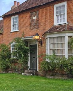 an old brick house with ivy growing on the windows and door, next to a green lawn