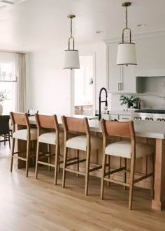 a kitchen island with four chairs in it and an island table next to it that has two lamps hanging from the ceiling