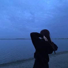 a woman is standing on the beach looking at the water