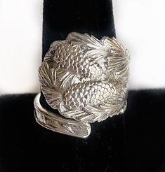 a silver ring sitting on top of a black velvet belt with pine cones in the center