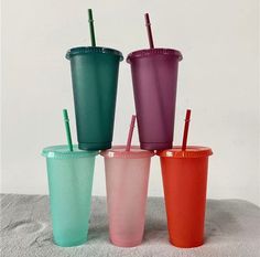 four different colored plastic cups with straws in them on a white surface and one is empty