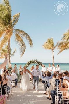 a bride and groom walking down the aisle to their wedding ceremony on the beach with palm trees