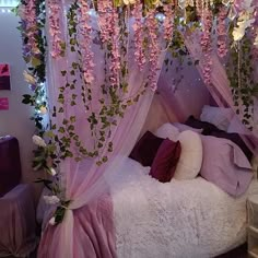 a canopy bed with pink flowers hanging from it's sides and pillows on the bottom