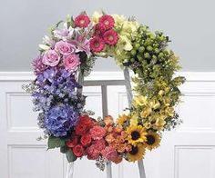 a colorful floral wreath on a stand in front of a door with white paneling