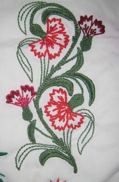 a white shirt with red and green flowers embroidered on the front, sitting on a bed