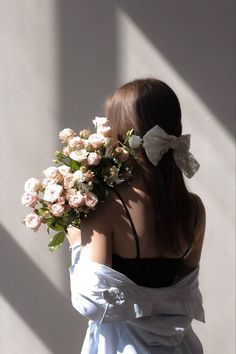 a woman with flowers in her hair is standing against a white wall and looking down at the ground