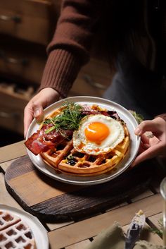 a person holding a plate with waffles, bacon and an egg on it