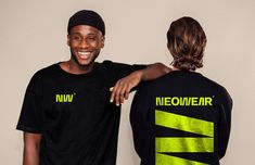 two men standing next to each other in front of a wall wearing black and neon green t - shirts