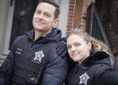 a man and woman standing next to each other in front of a brick building wearing police uniforms