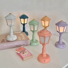 four different colored lamps sitting on top of a table next to a book and lamp