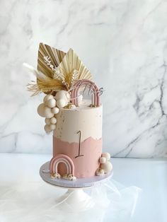 a pink and white cake with gold decorations on top, sitting on a marble table